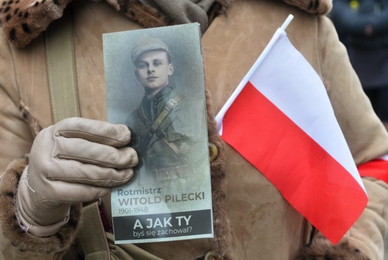 Zdjęcie rotmistrza Witolda Pileckiego trzymane przez kobietę. Polska flaga