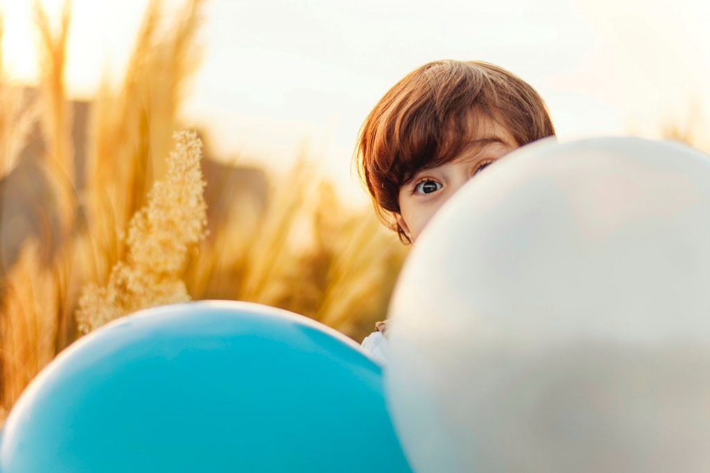 Chłopiec chowający się za balonami, otwarta przestrzeń