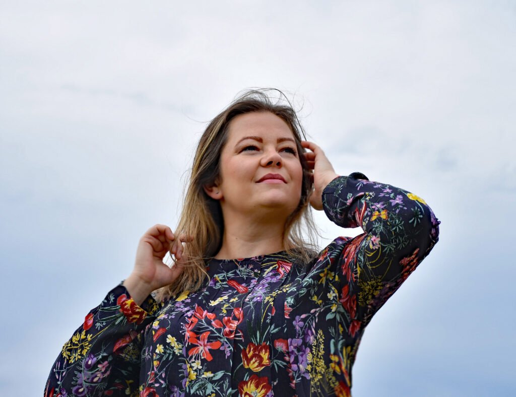 Magdalena Bańkowska-Moskwa ubrana w sukienkę w kwiaty na tle nieba