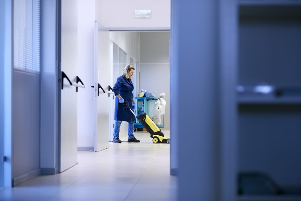 Branża sprzątająca: Groźby utraty pracy w przypadku choroby Kobieta w średnim wieku sprzątająca pomieszczenie publiczne, sprzątaczka z industrialnym odkurzaczem.