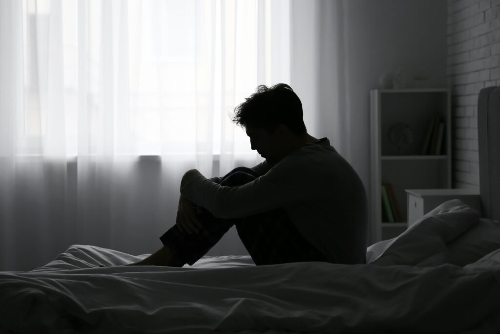 Norwegia: wzrost zaburzeń psychicznych Smutny, chory, depresja. Mężczyzna siedzi na łóżku ze spuszczoną głową.